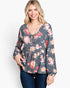 A woman wearing a long-sleeve floral tie-front top in dark gray with pink, red, and peach flowers, paired with dark blue jeans, against a plain white background.
