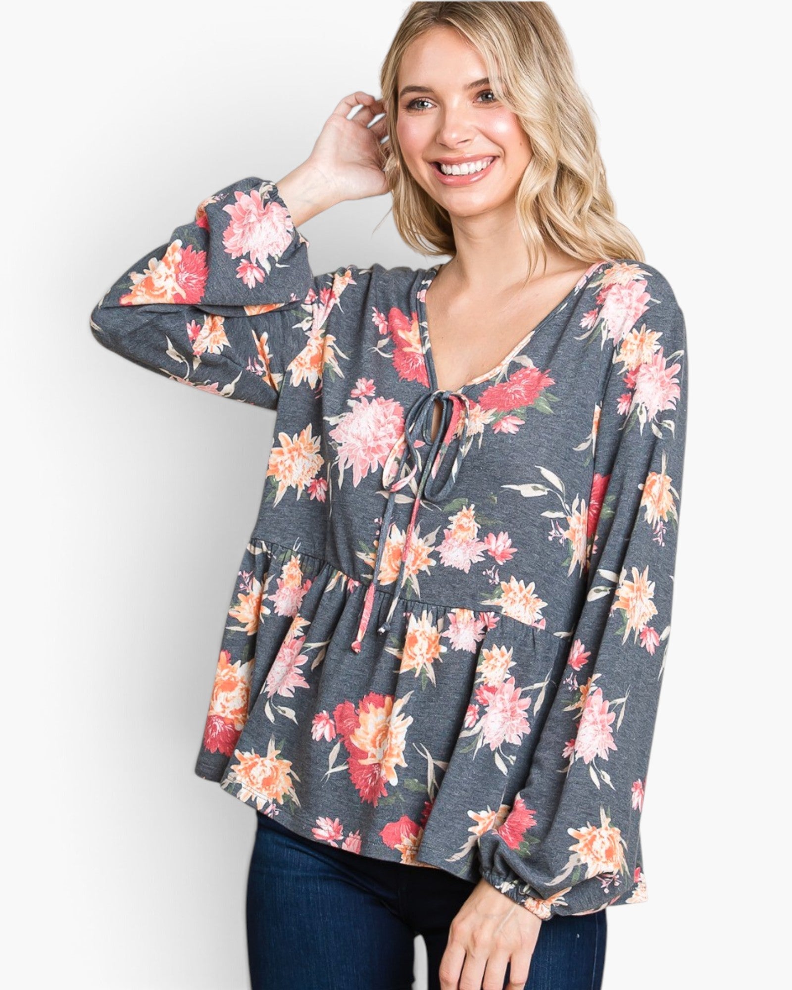 A woman wearing a dark gray long-sleeve blouse with a vibrant pink, red, and orange floral print, paired with dark blue jeans, against a plain white background.