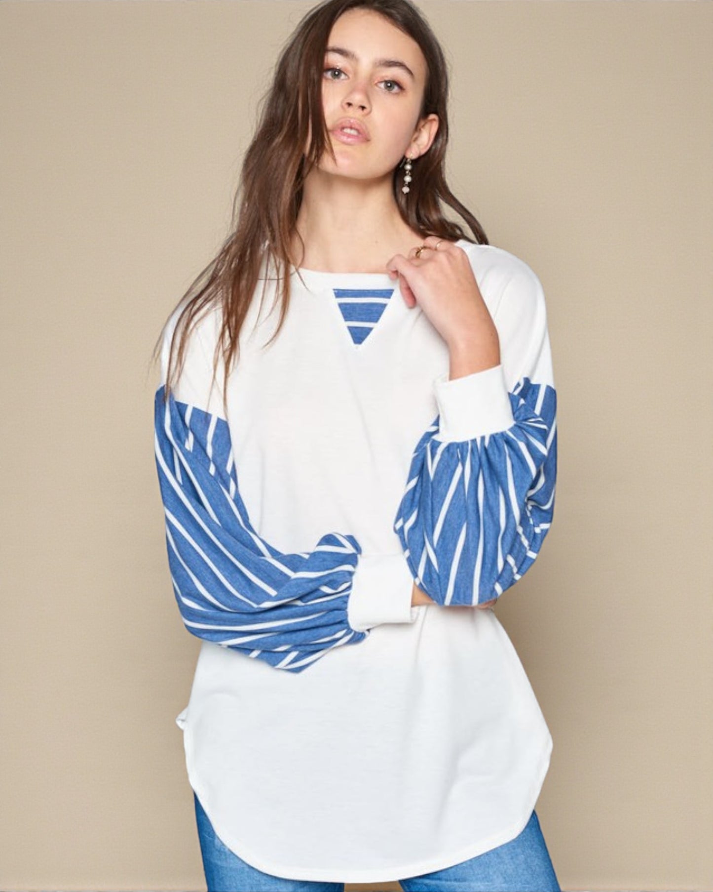 Woman wearing a white top with blue patterned sleeves against a beige background