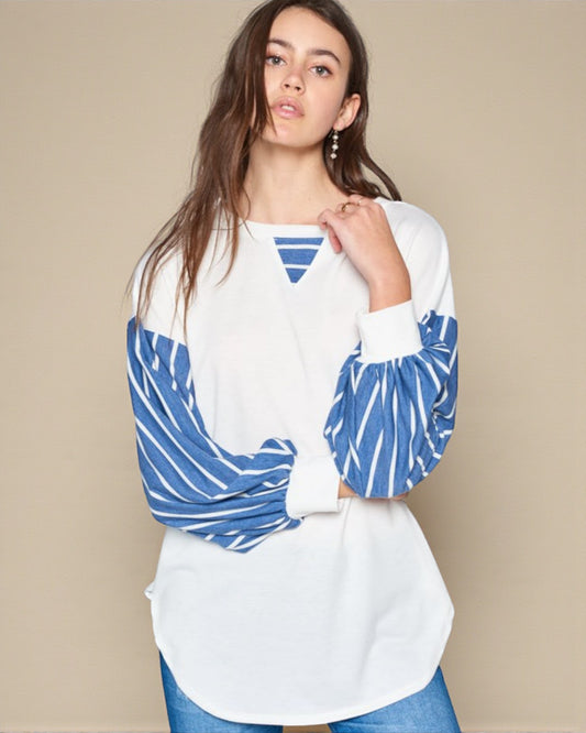 Woman wearing a white top with blue patterned sleeves against a beige background