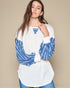 Woman wearing a white top with blue patterned sleeves against a beige background