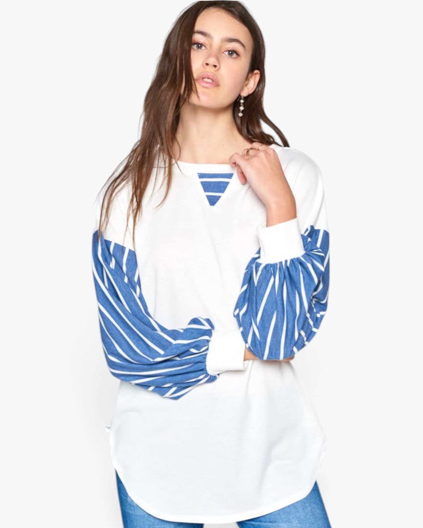A woman modeling a white long-sleeve top with blue and white striped balloon sleeves and a blue striped V-neckline detail, paired with blue jeans against a plain white background.