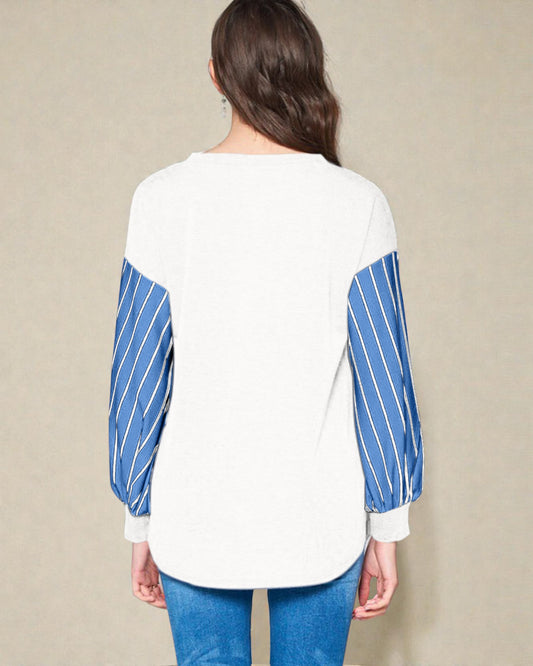 Person wearing a white top with blue striped sleeves against a beige background