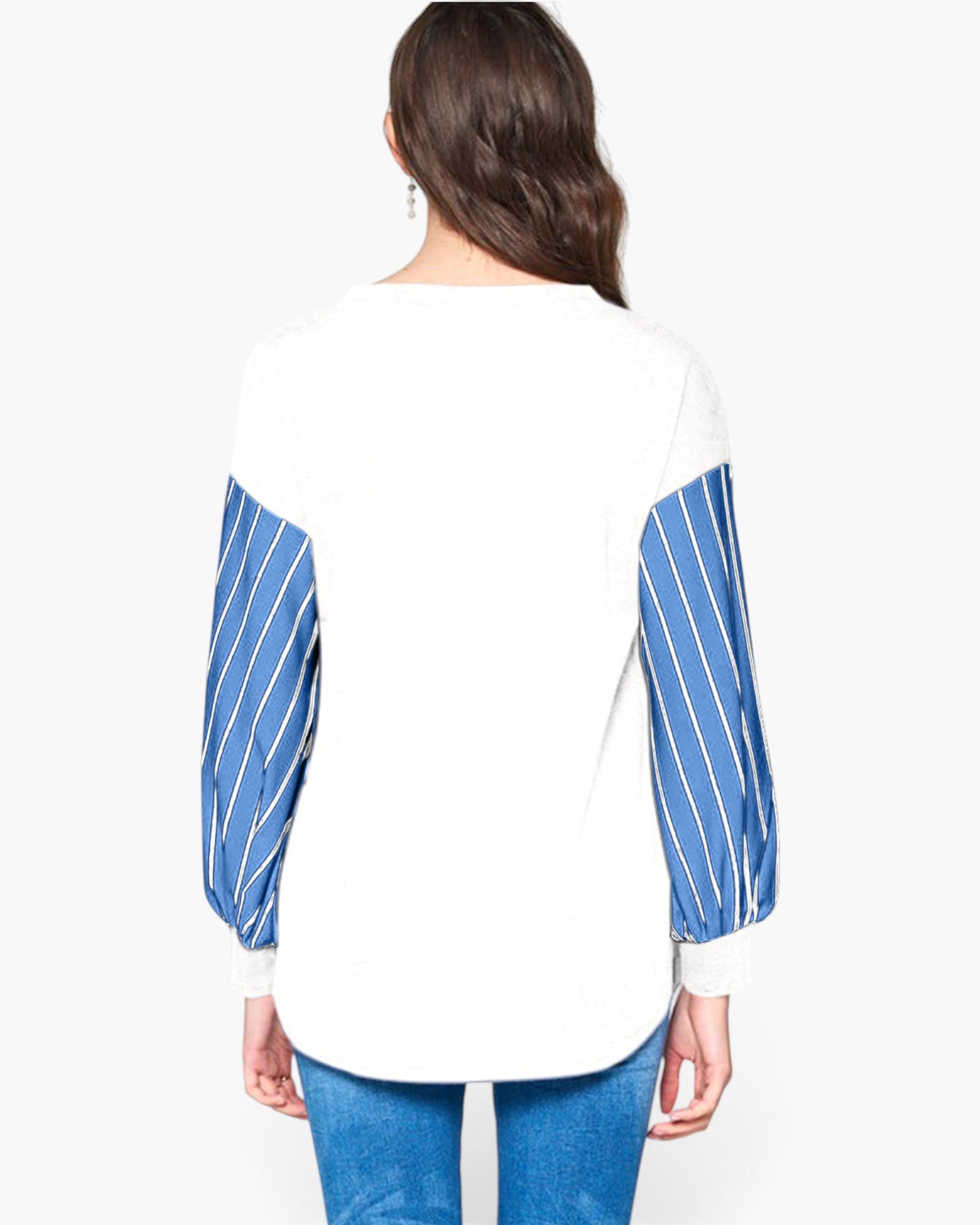 A woman viewed from the back wearing a white long-sleeve top with blue and white striped sleeves, paired with blue jeans, against a plain light gray studio background.