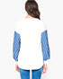 A woman viewed from the back wearing a white long-sleeve top with blue and white striped sleeves, paired with blue jeans, against a plain light gray studio background.