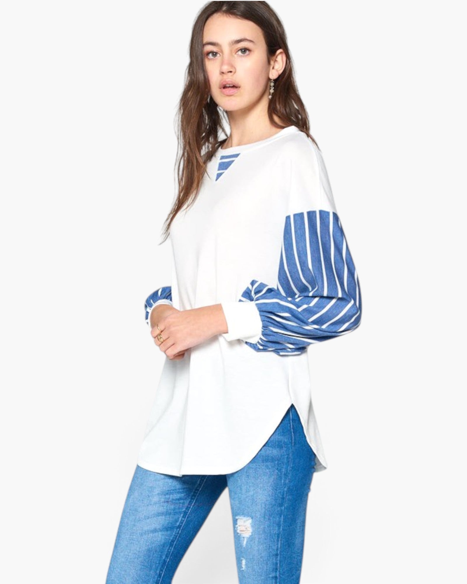 A woman modeling a white long-sleeve top with blue and white striped puff sleeves, paired with blue jeans, against a plain white background.