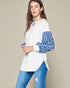Woman wearing a white top with blue striped sleeves and blue jeans on a beige background