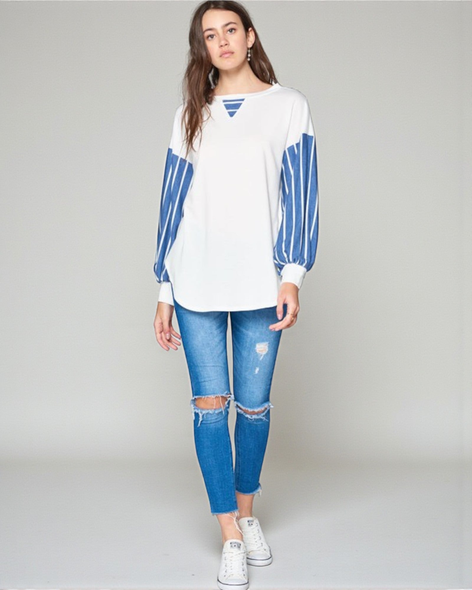 Woman wearing a white and blue striped long-sleeve shirt with ripped jeans on a plain background