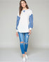 Woman wearing a white and blue striped long-sleeve shirt with ripped jeans on a plain background