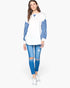 A woman modeling a white long-sleeve top with blue striped sleeves, paired with distressed blue jeans and white sneakers, against a plain white background.