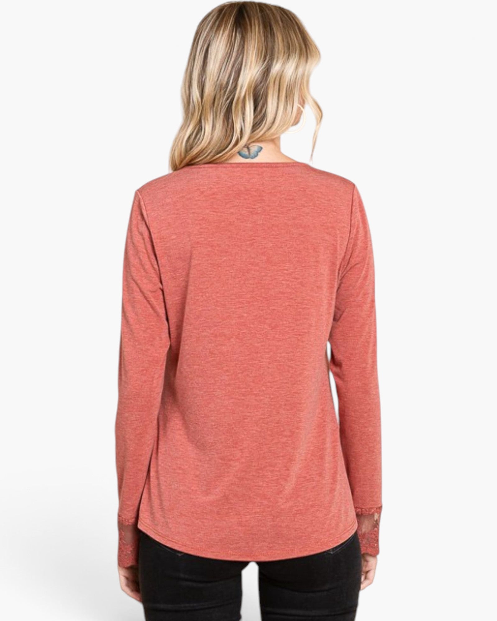 A woman viewed from the back wearing a heathered coral pink long-sleeve top and black pants, against a plain white background.