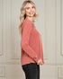 Woman wearing a pink long-sleeve top against a neutral wall.