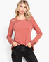 A woman modeling a dusty rose long-sleeve top with sheer lace detailing on the shoulders and cuffs, paired with black jeans, against a plain white background.