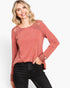 A woman wearing a dusty rose long-sleeve top with lace detailing on the shoulders and cuffs, paired with black jeans, against a plain white background.
