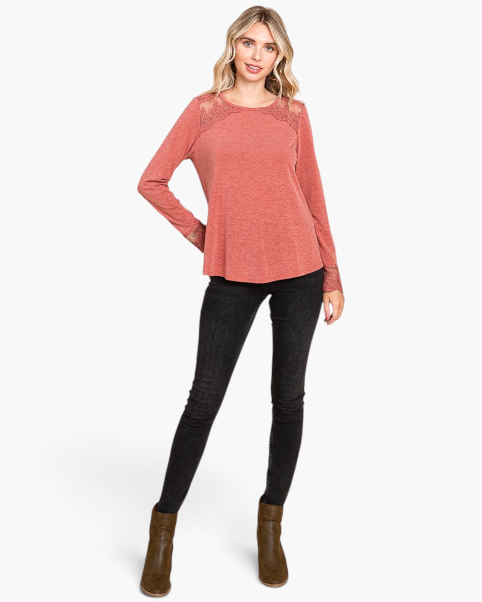 A woman modeling a long-sleeve heathered coral pink top with lace shoulder panels, paired with black skinny jeans and brown ankle boots, against a plain white background.