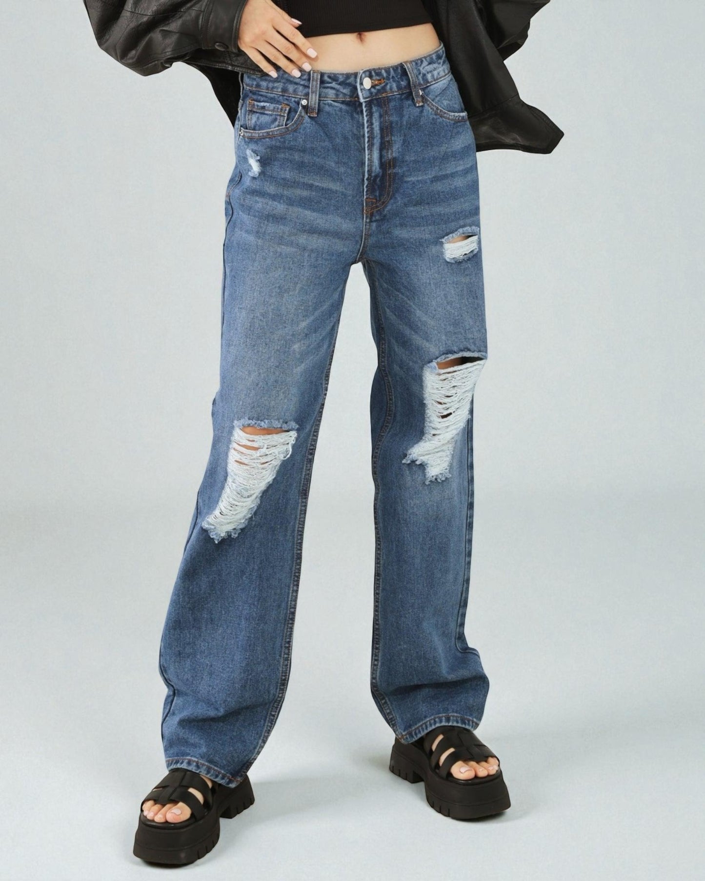 Person wearing distressed blue jeans on a plain background