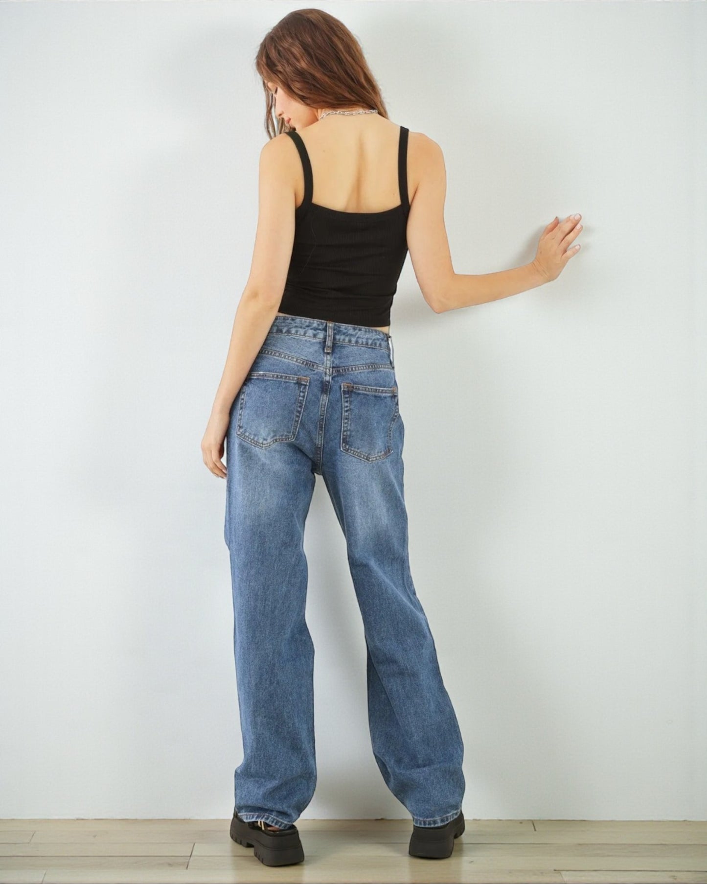 Woman wearing blue jeans and a black tank top against a white wall.