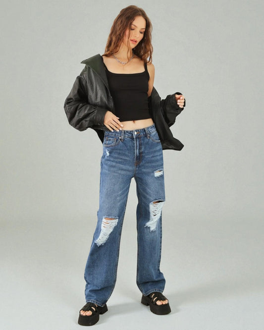 Woman wearing a black leather jacket, black crop top, and blue distressed jeans on a gray background