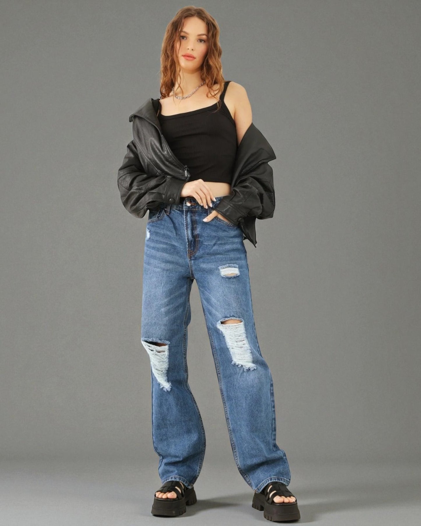 Woman wearing a black off-shoulder top and ripped blue jeans against a gray background