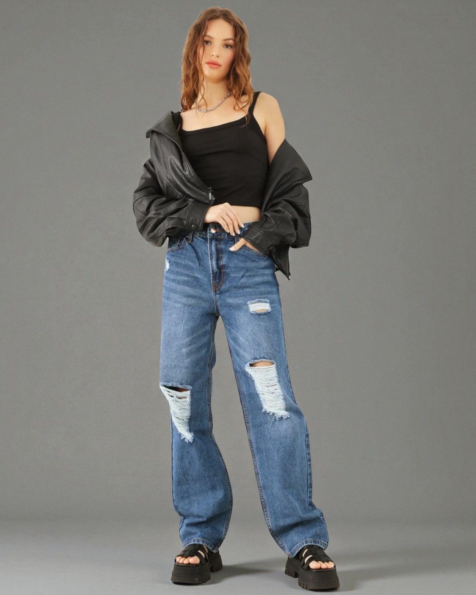 Woman wearing a black off-shoulder top and ripped blue jeans against a gray background