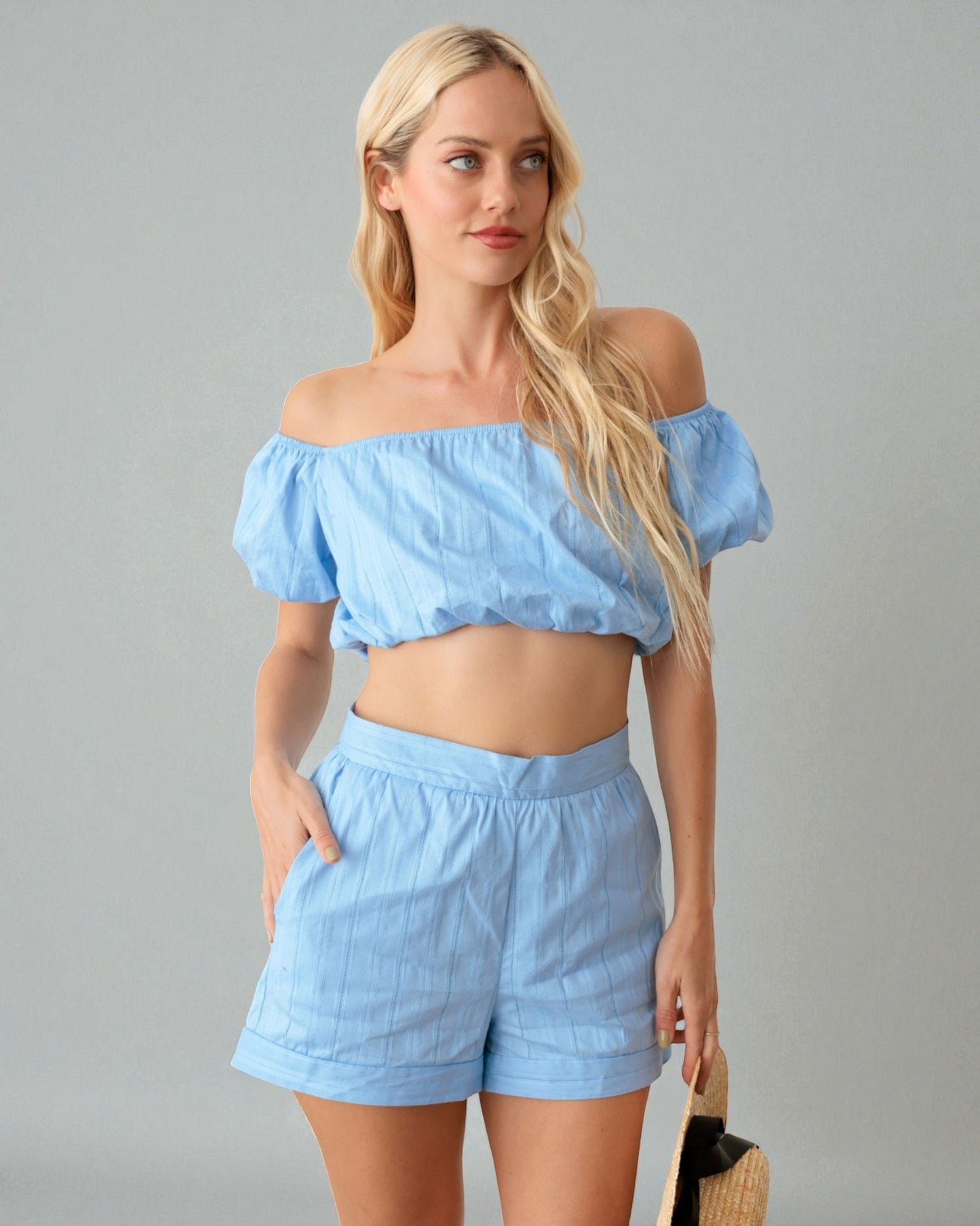 Woman wearing a light blue off-shoulder top and shorts set against a gray background