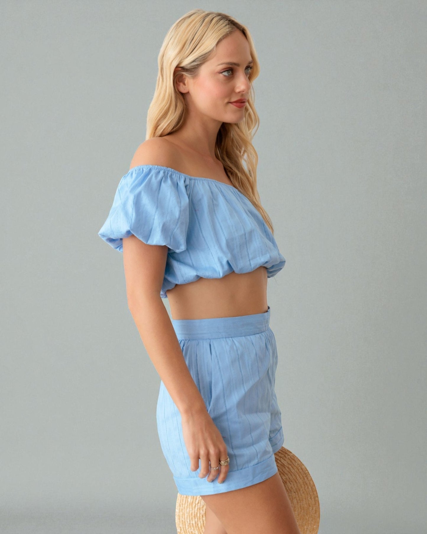 Woman wearing a light blue off-shoulder top and shorts set against a gray background