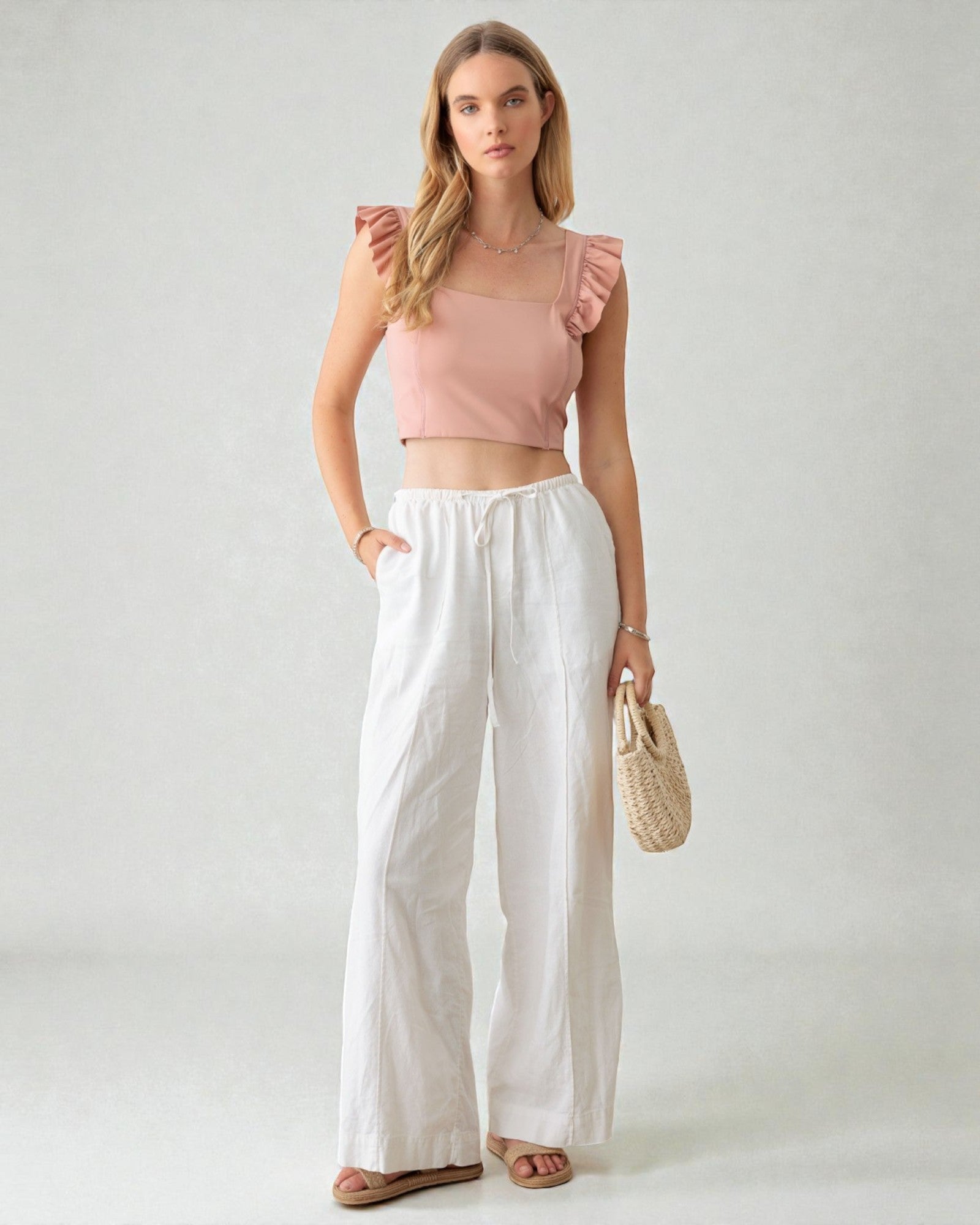 Woman wearing a pink top and white pants against a plain background