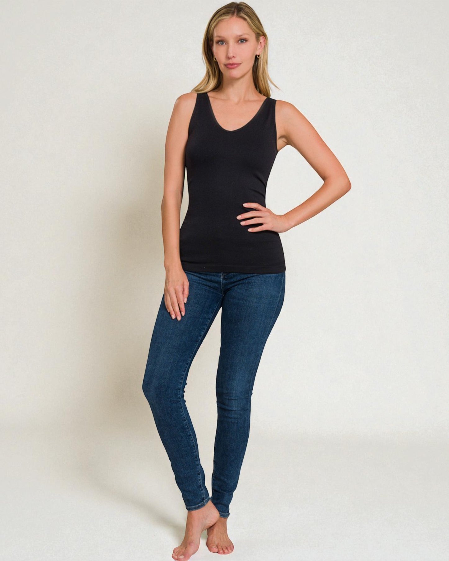 Woman wearing a black tank top and blue jeans on a white background