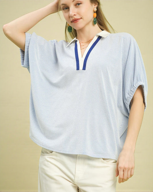 Woman wearing a light blue striped shirt with a white collar against a beige background