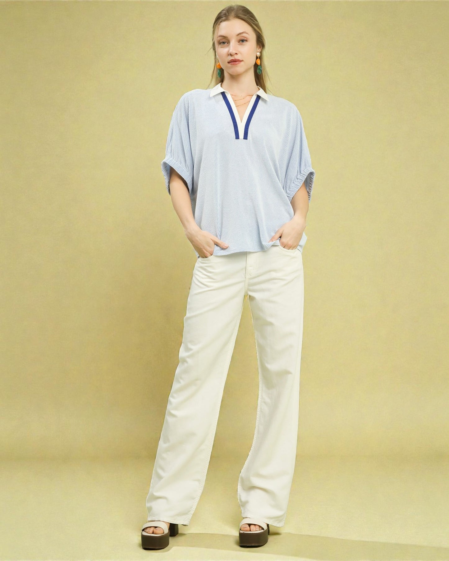 Woman wearing a light blue top and white pants on a beige background