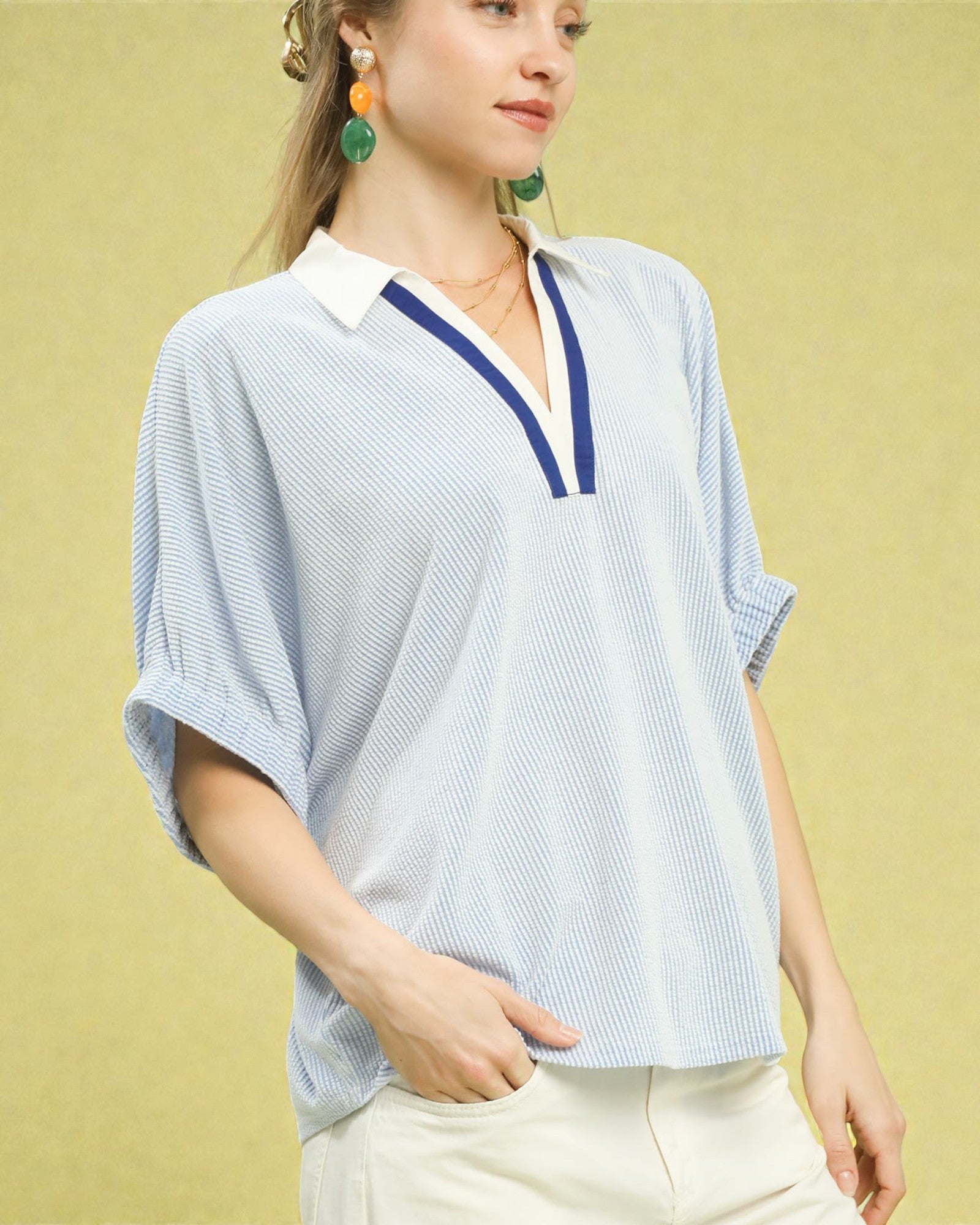 Woman wearing a light blue striped shirt with a white collar against a yellow background