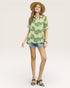 Woman wearing a green floral shirt and denim shorts on a white background