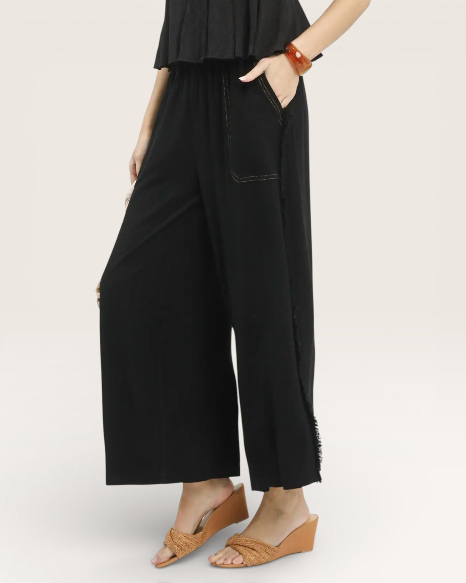 Person wearing black wide-leg pants and brown sandals on a white background