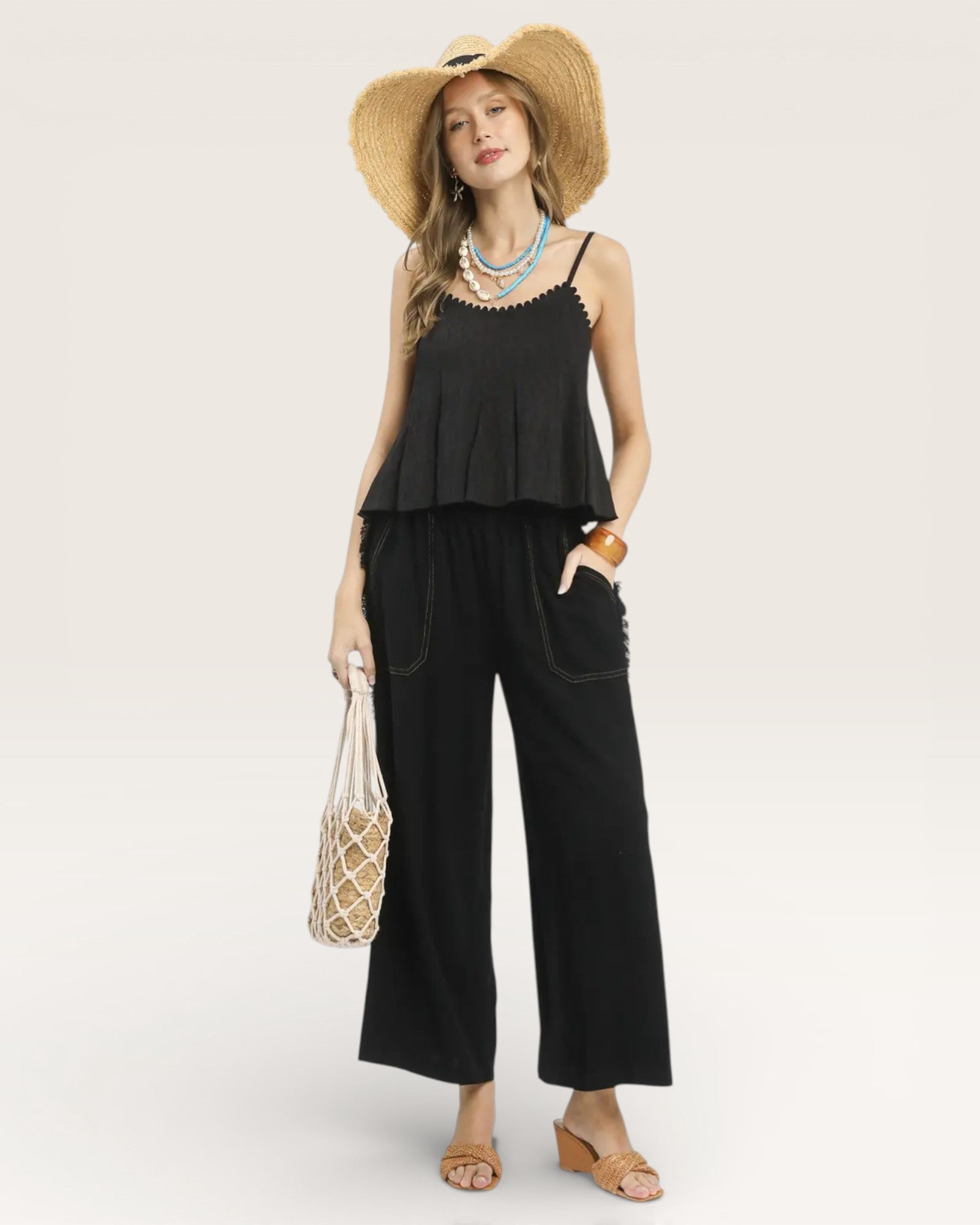 Woman wearing a black sleeveless top and wide-leg pants with a straw hat on a white background