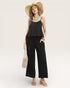 Woman wearing a black sleeveless top and wide-leg pants with a straw hat on a white background
