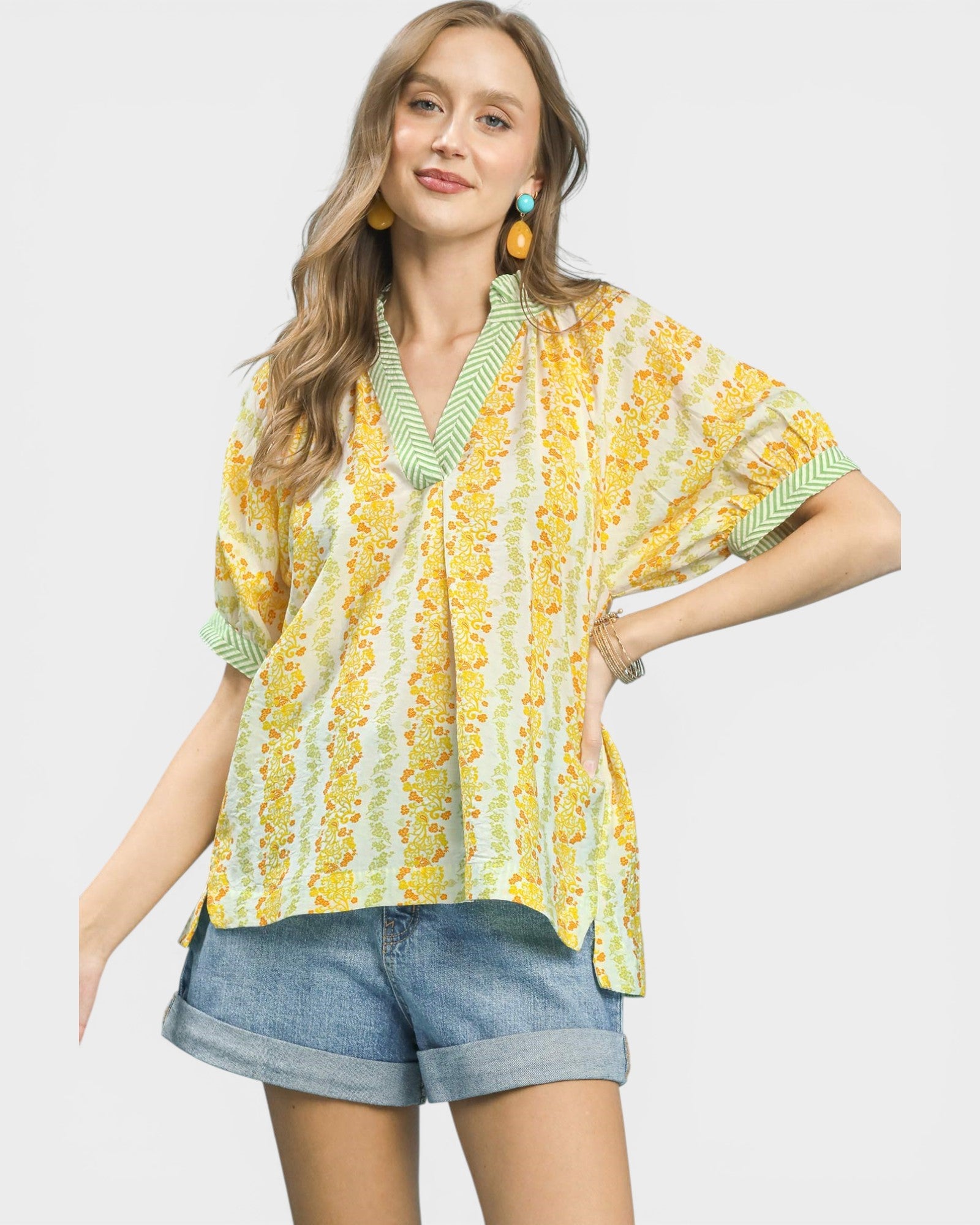 Woman wearing a yellow and green patterned blouse with denim shorts on a white background