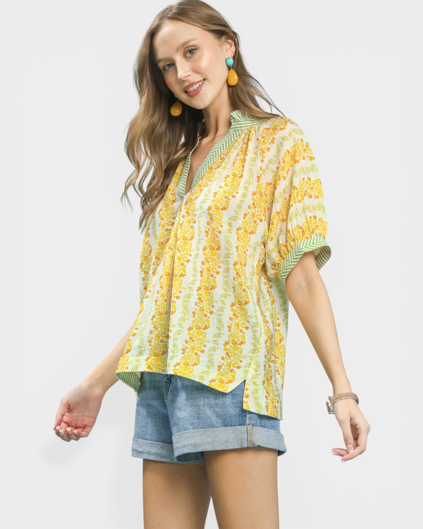 Woman wearing a yellow and green patterned top with denim shorts on a white background