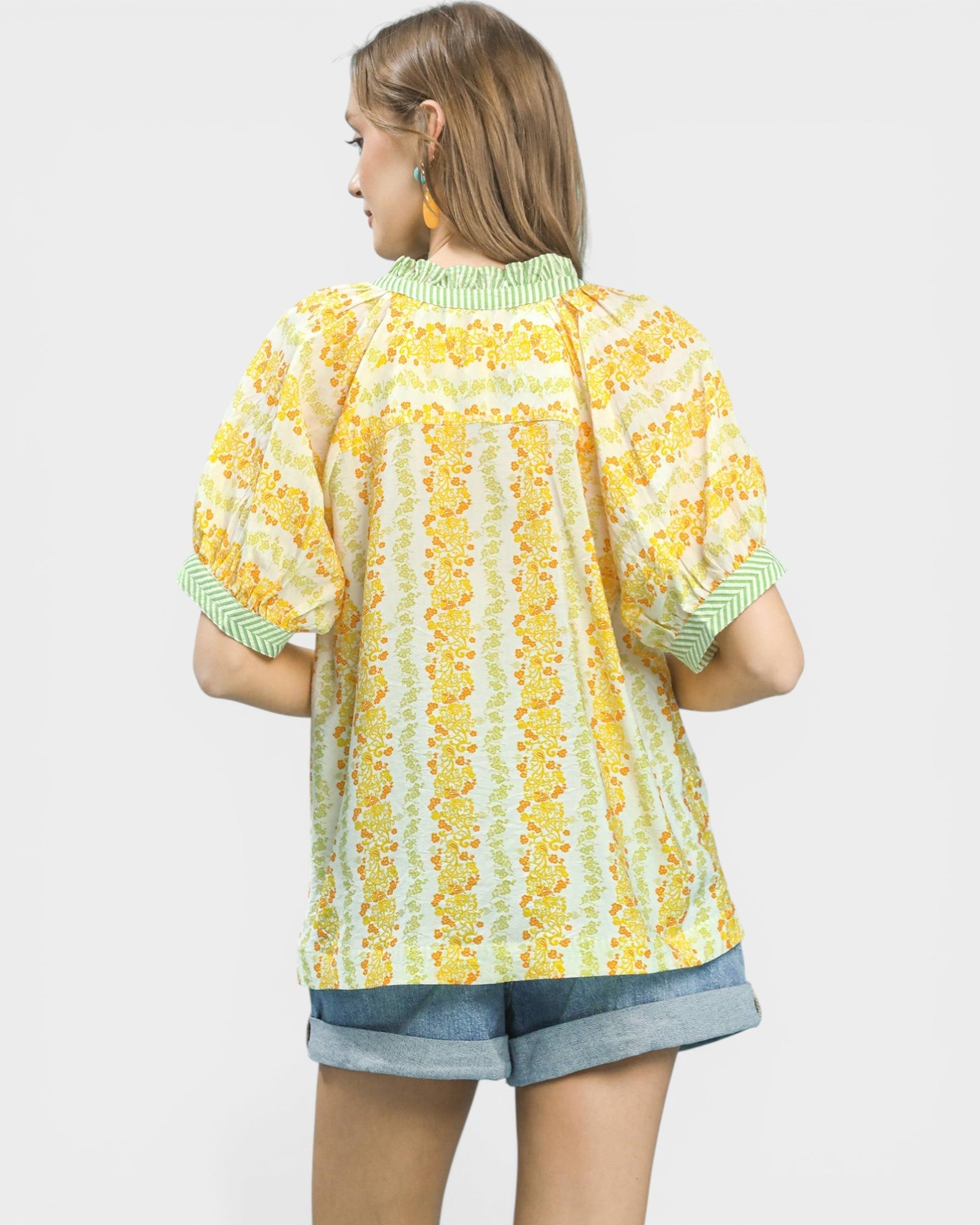 Woman wearing a yellow floral blouse with green trim on a white background
