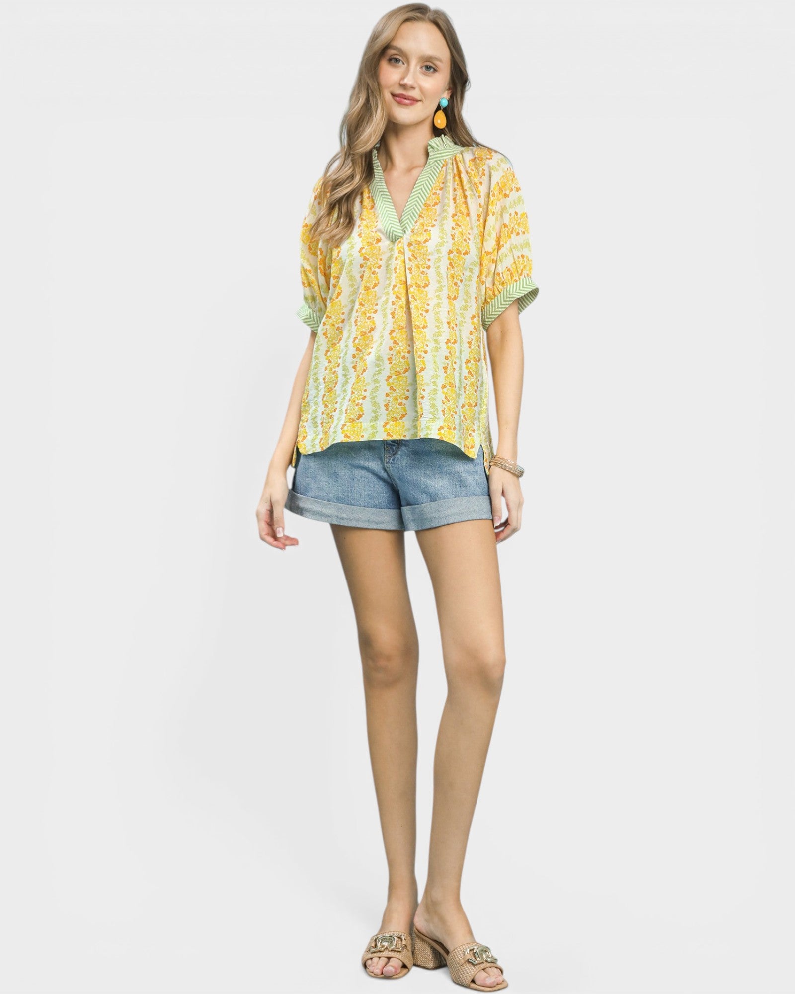 Woman wearing a yellow patterned blouse and denim shorts on a white background