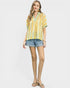 Woman wearing a yellow patterned blouse and denim shorts on a white background