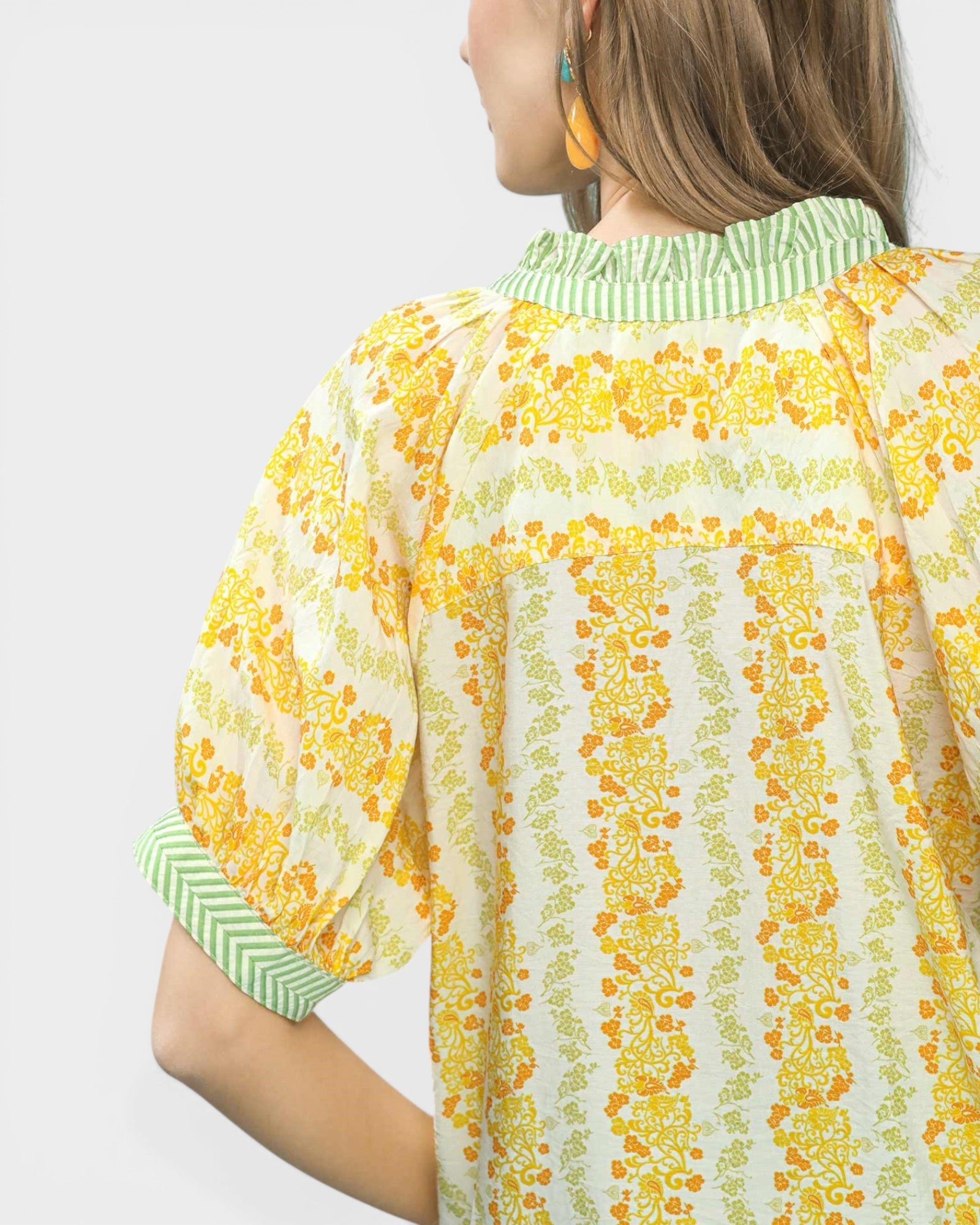 Woman wearing a yellow floral blouse with green trim on a white background