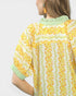 Woman wearing a yellow floral blouse with green trim on a white background