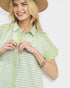 Woman wearing a green and white checkered shirt with a beige hat on a light gray background