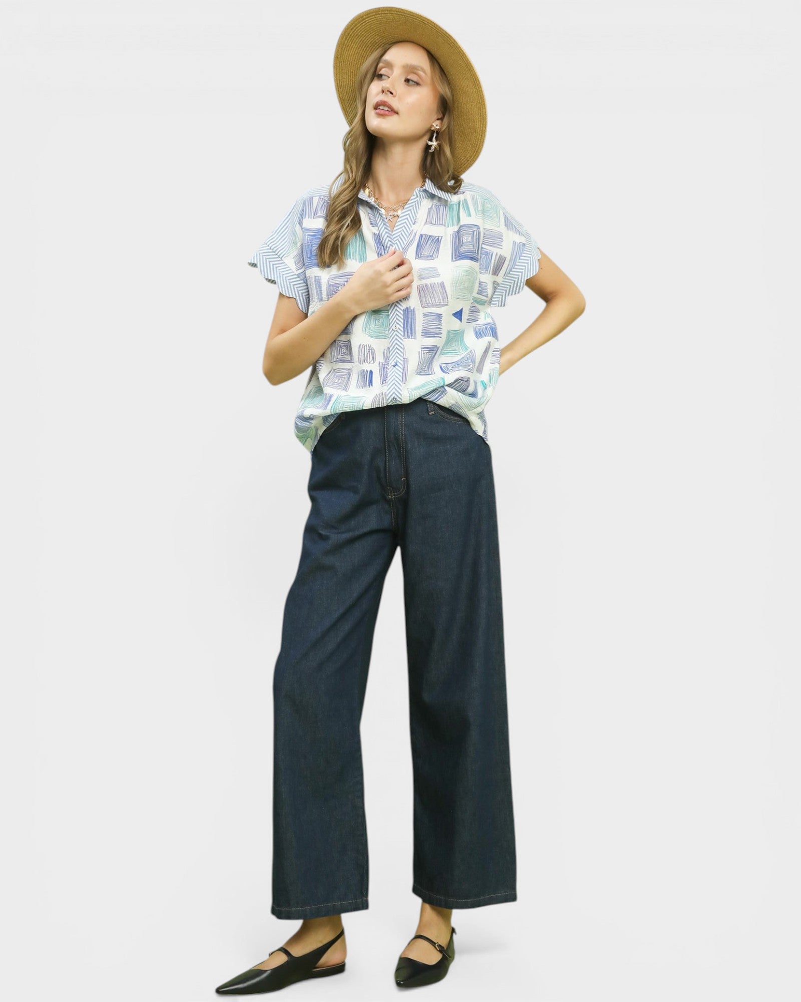 Woman wearing a patterned shirt and wide-leg pants with a straw hat on a white background