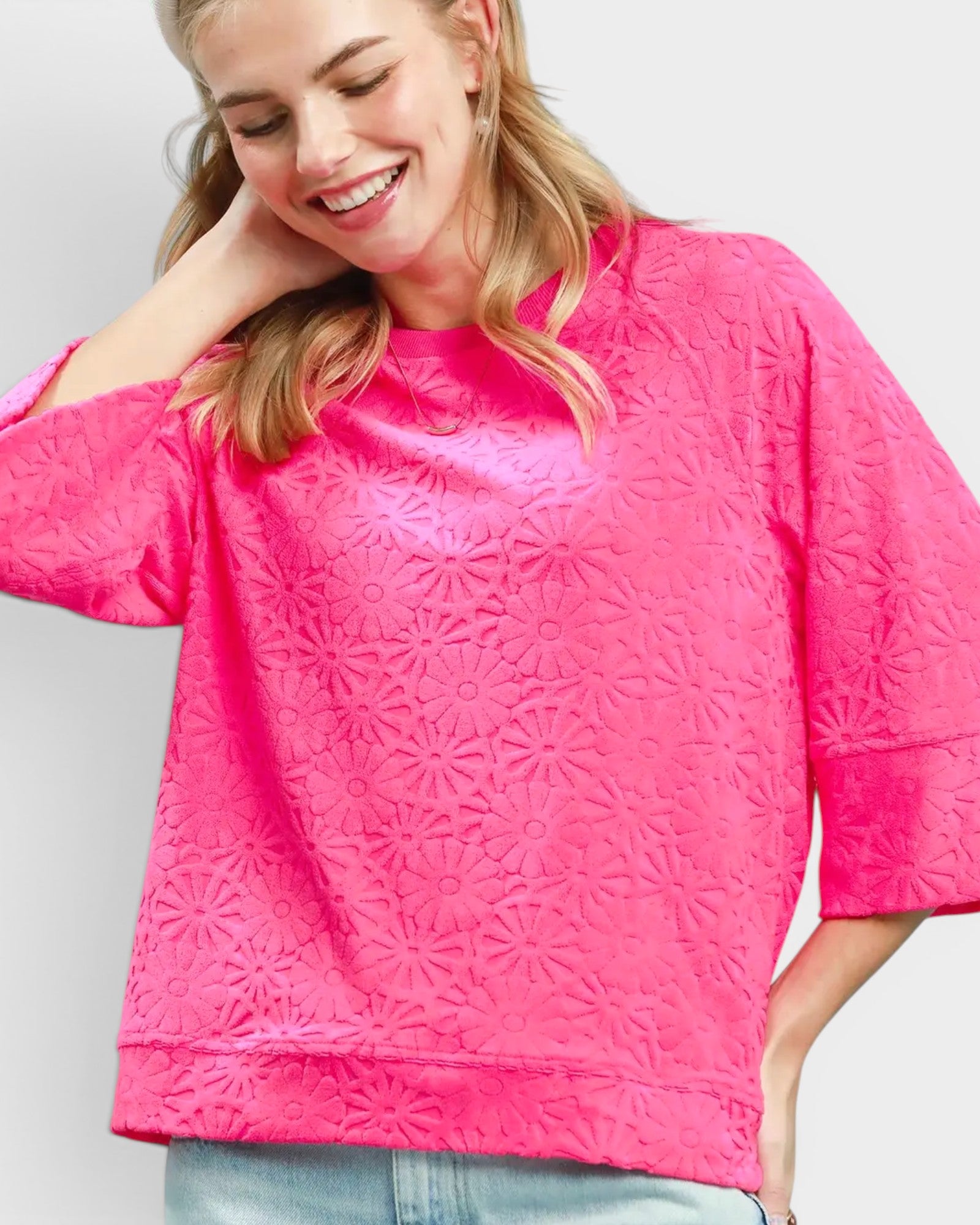 Woman wearing a bright pink textured top against a plain background