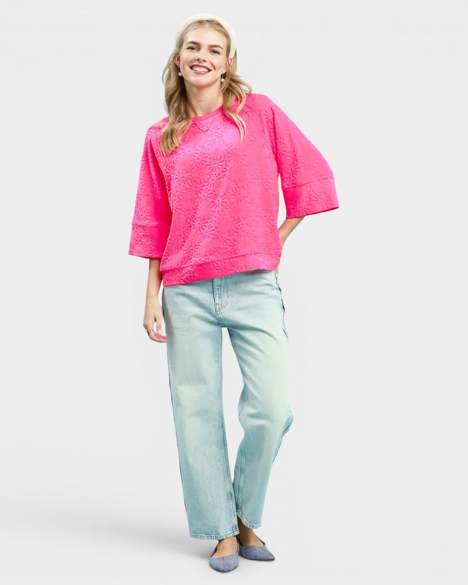 Woman wearing a bright pink top and light blue jeans on a white background