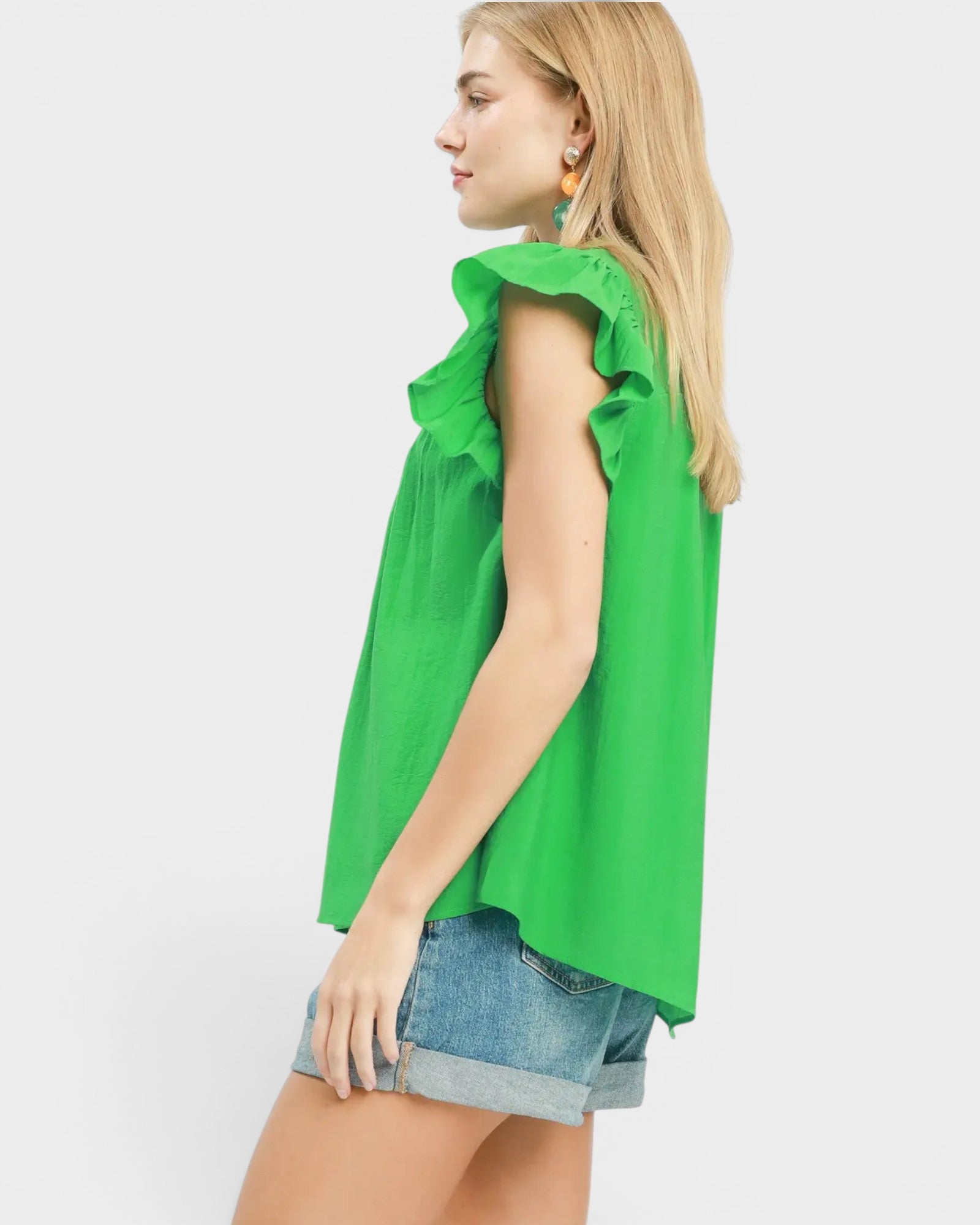 Woman wearing a green sleeveless top with ruffled details on a white background