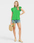Woman wearing a green blouse and denim shorts, holding a straw bag with flowers on a white background