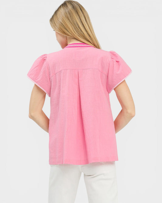 Person wearing a pink blouse with ruffled sleeves on a light gray background