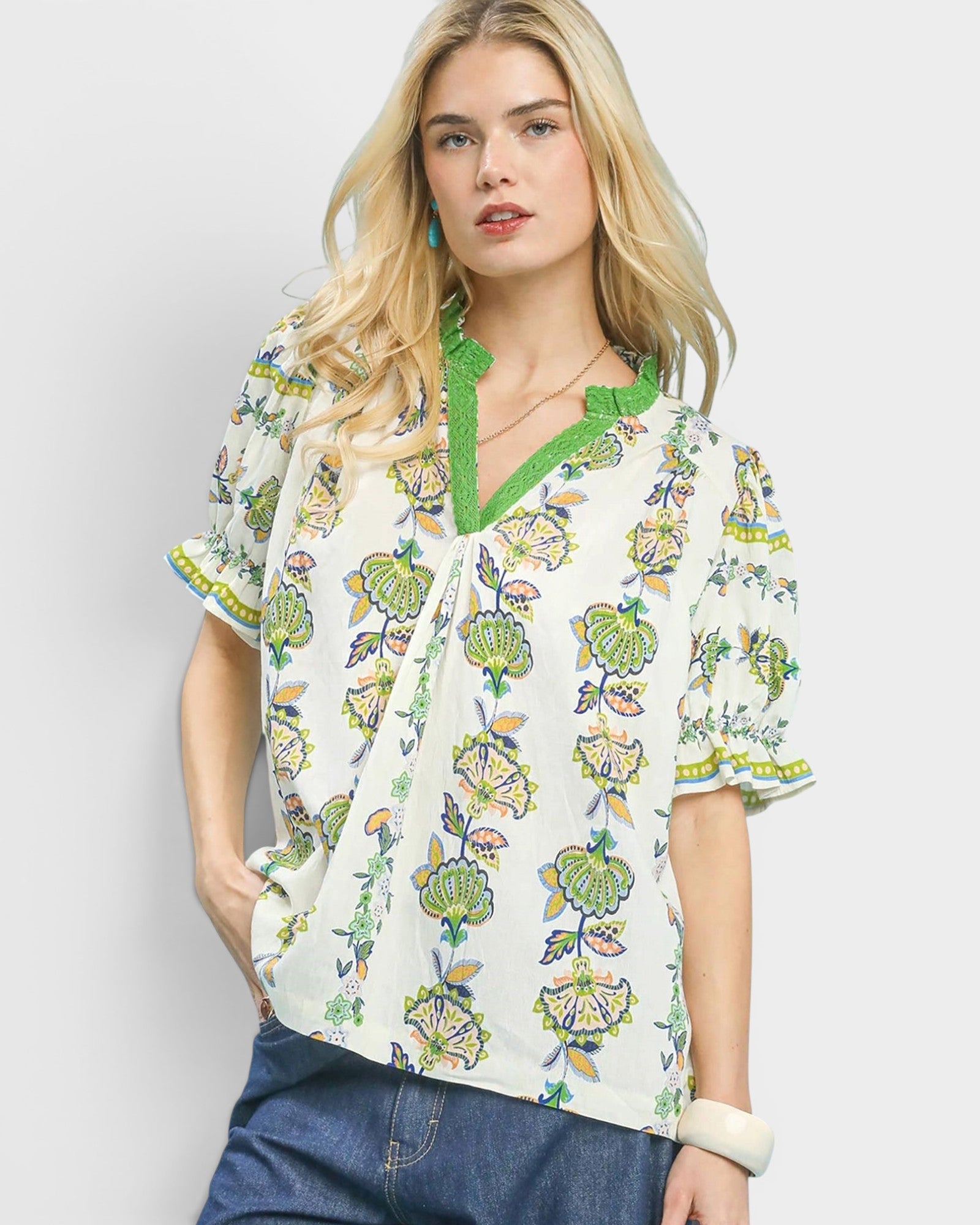 Woman wearing a floral blouse with green trim on a plain background